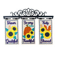 Three vertical decorative garden flags hanging from a black metal scrollwork bracket. The flags feature autumn-themed designs: the left says 'Forever Grateful' with yellow sunflowers, the center says 'So very Thankful' with a pumpkin and sunflowers, and the right says 'Truly Blessed' with sunflowers and autumn leaves.