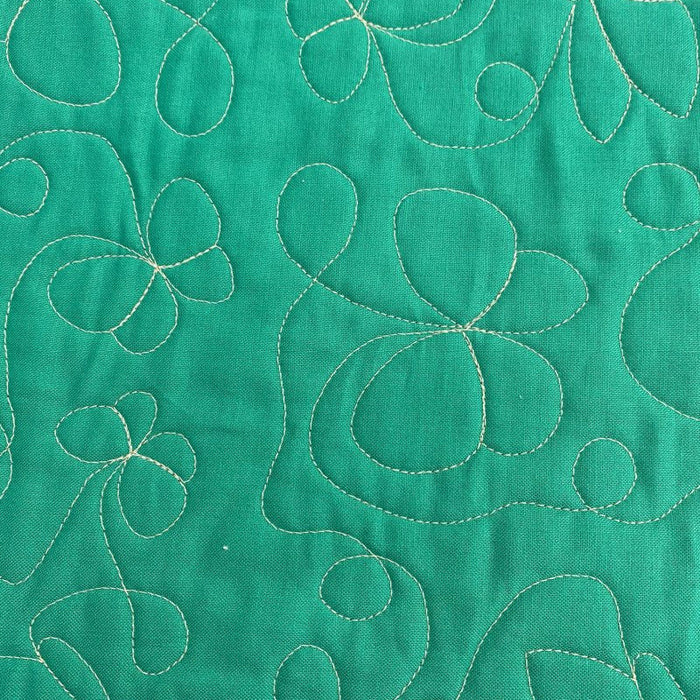 A close-up of a green quilted fabric featuring stitched floral and abstract leaf patterns in a contrasting light beige or cream thread.