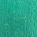 A close-up of a green quilted fabric featuring stitched floral and abstract leaf patterns in a contrasting light beige or cream thread.