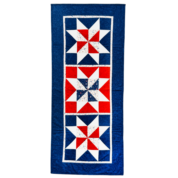 A vintage-style quilt runner featuring three vertical panels with red, white, and blue starburst patterns, finished with a wide blue border.