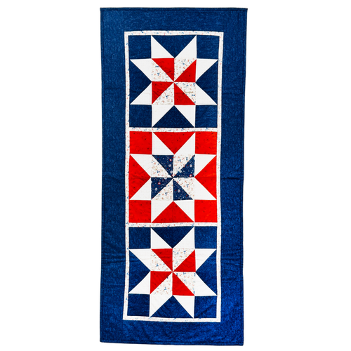 A vintage-style quilt runner featuring three vertical panels with red, white, and blue starburst patterns, finished with a wide blue border.