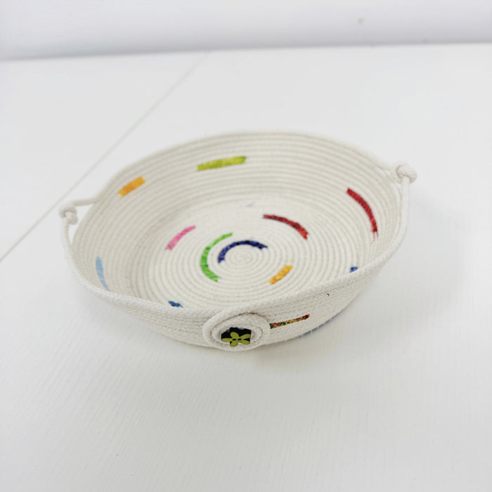A small woven basket tray made from off-white rope, decorated with colorful embroidered curved lines and small dots in red, green, blue, yellow, and pink, set against a plain white background.